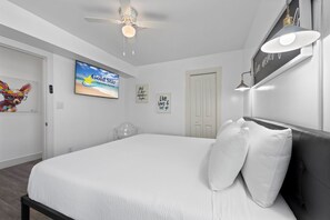 A bedroom with a bed, a ceiling fan, a TV, and wall art. - Pipedreams West (Gulf Shores)