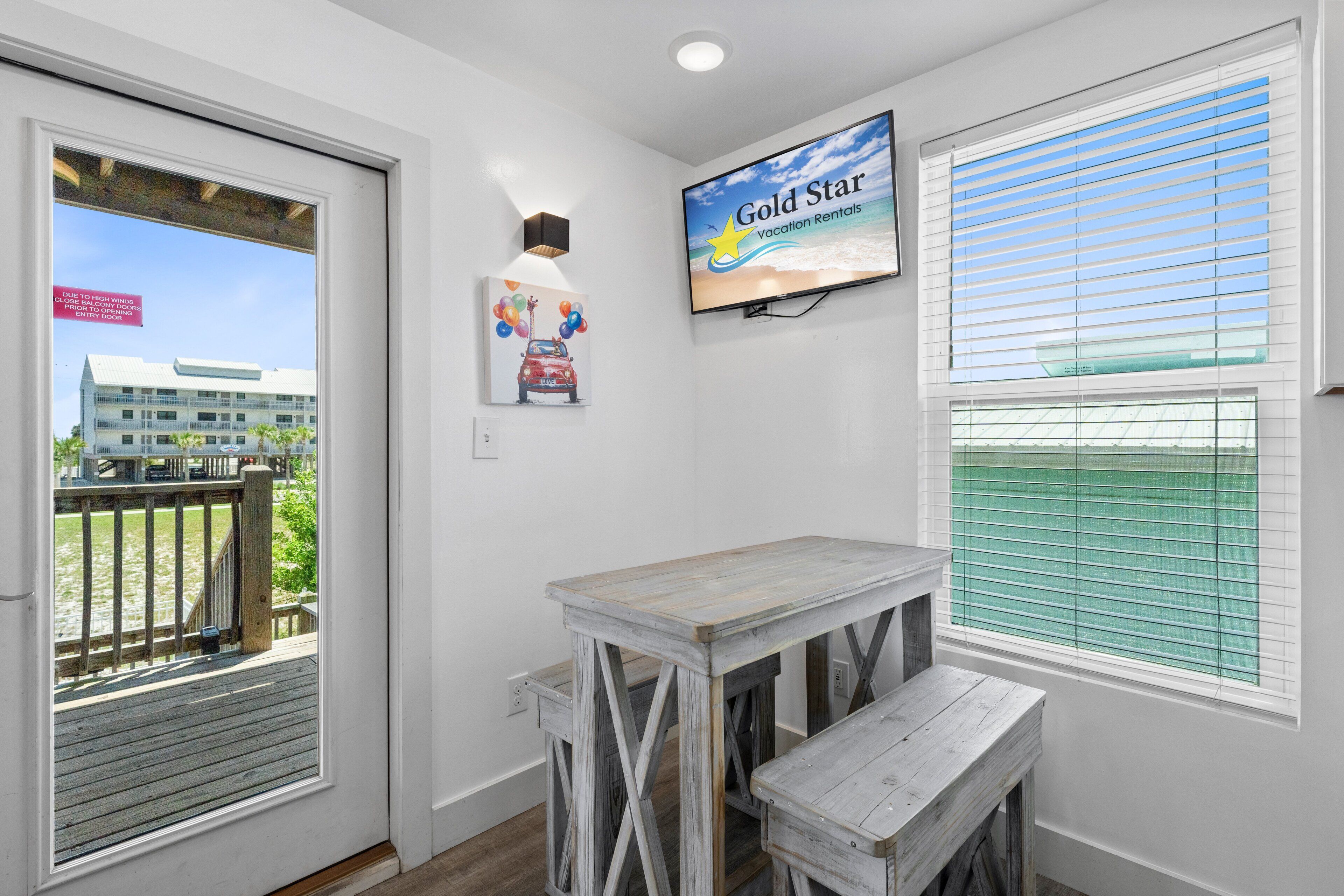 Una habitación con una mesa de madera y un banco, un televisor montado en la pared y una ventana con persianas.
