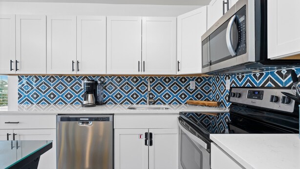 Uma cozinha moderna com armários brancos, lava-louças de aço inoxidável, micro-ondas e painel de fundo estampado.