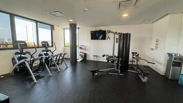 Ein Fitnessstudio mit Cardiogeräten, Gewichten und einem Fernsehbildschirm.