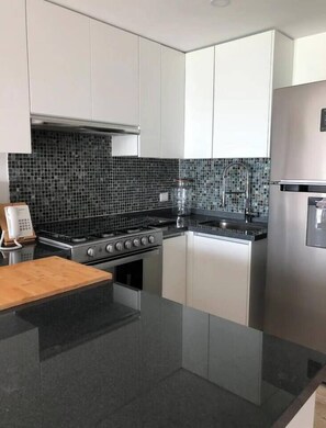 Una cocina moderna con estufa a gas, electrodomésticos de acero inoxidable y un salpicadero de azulejos negros.