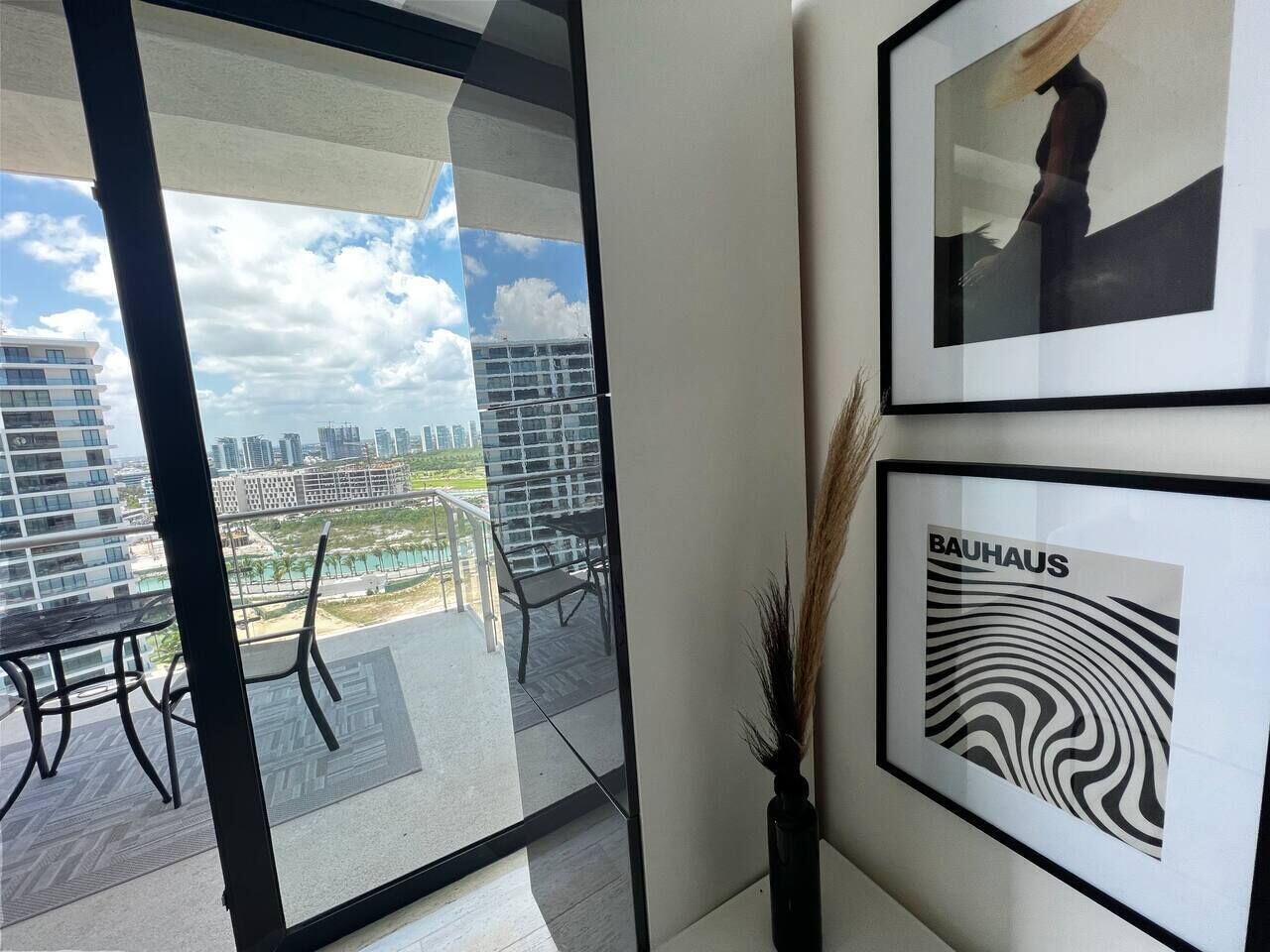 Un intérieur moderne avec un balcon, des œuvres d’art encadrées et une vue sur le paysage urbain.