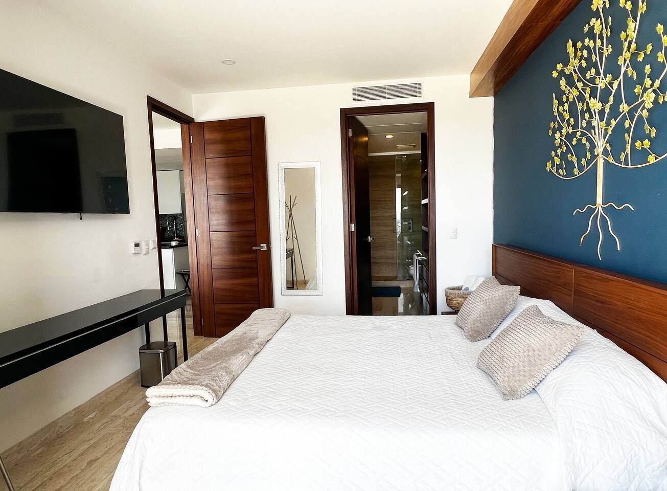 Ein Schlafzimmer mit einem großen Bett, einem an der Wand befestigten Fernseher und einem hölzernen Kopfteil.