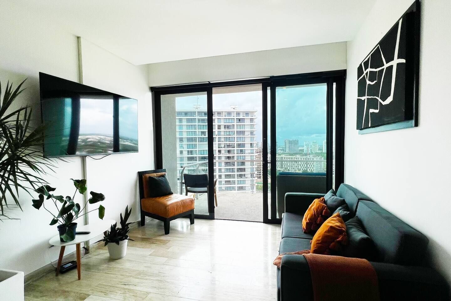 Ein modernes Wohnzimmer mit einer Couch, einem Sessel, einem Fernseher und einem großen Fenster mit Blick auf die Stadt.