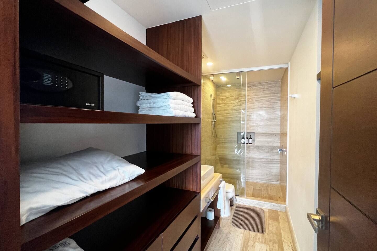 Un baño pequeño con cabina de ducha de vidrio, repisas de madera con toallas y un inodoro.