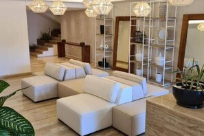 Ein modernes Wohnzimmer mit einem Ecksofa, einer Glastrennwand und einer Treppe im Hintergrund.