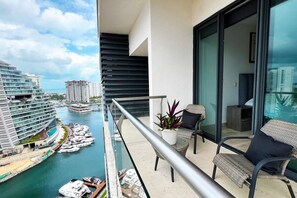 Ein Balkon mit Blick auf einen Yachthafen, ein Essbereich mit Stühlen und einem Tisch sowie ein großes Fenster.