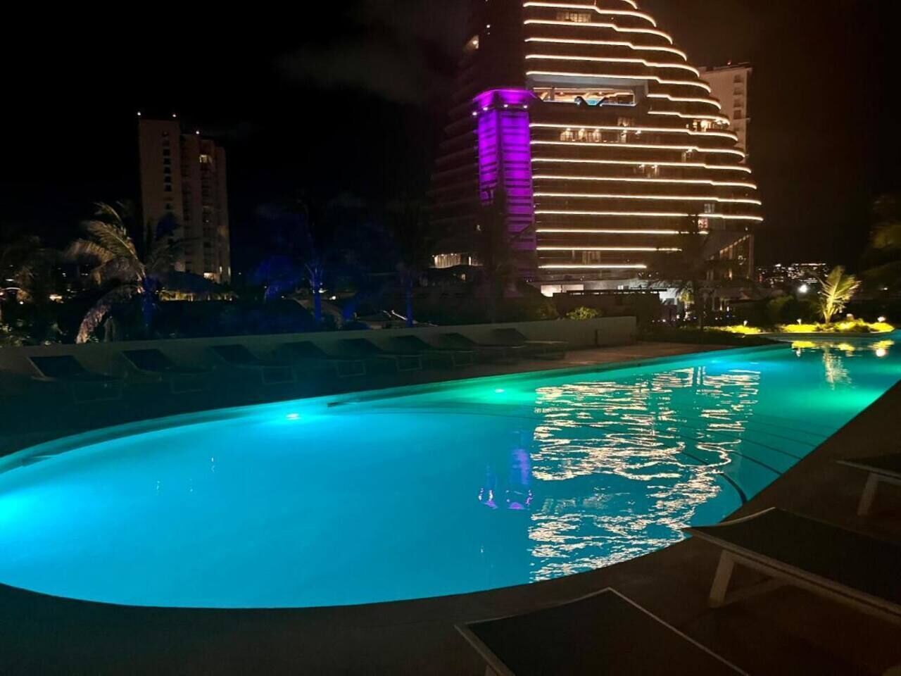 Ein Schwimmbad bei Nacht mit einem modernen Gebäude im Hintergrund.