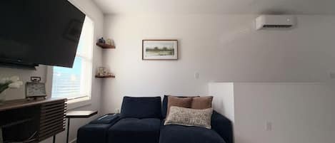 A living room with a sectional sofa, a flat-screen TV mounted on the wall, and a framed picture above the sofa.