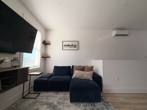 Ein Wohnzimmer mit Ecksofa, einem flachbildfernseher an der Wand und einem gerahmten Bild über der Couch.