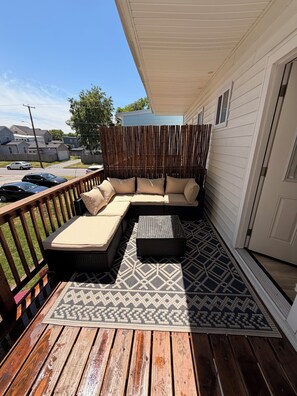 Eine überdachte Terrasse mit einer Eckcouch, einem kleinen Tisch und einem gemusterten Teppich.