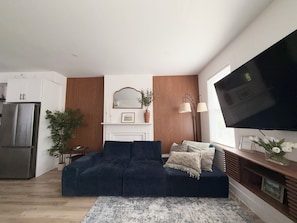 Ein modernes Wohnzimmer mit einer Couch, einem Flachbildfernseher, einem Kamin und einer Küchenzeile.