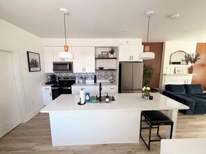 A modern kitchen with white cabinetry, a central island, and pendant lighting. - Newly renovated Church Hill retreat with private balcony & coffeehouse next door (Richmond)