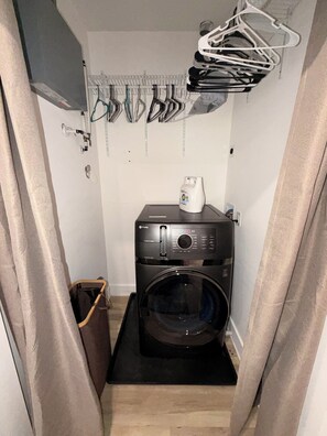 A laundry room with a front-loading washer and dryer, a hanging rack for clothes, and a trash bin. - Newly renovated Church Hill retreat with private balcony & coffeehouse next door (Richmond)