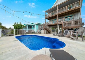 A swimming pool with a wooden deck, lounge chairs, and string lights. - Pipedreams East (Gulf Shores)