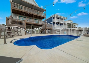 A swimming pool with a wooden deck, a multi-level building with balconies, and string lights. - Pipedreams East (Gulf Shores)