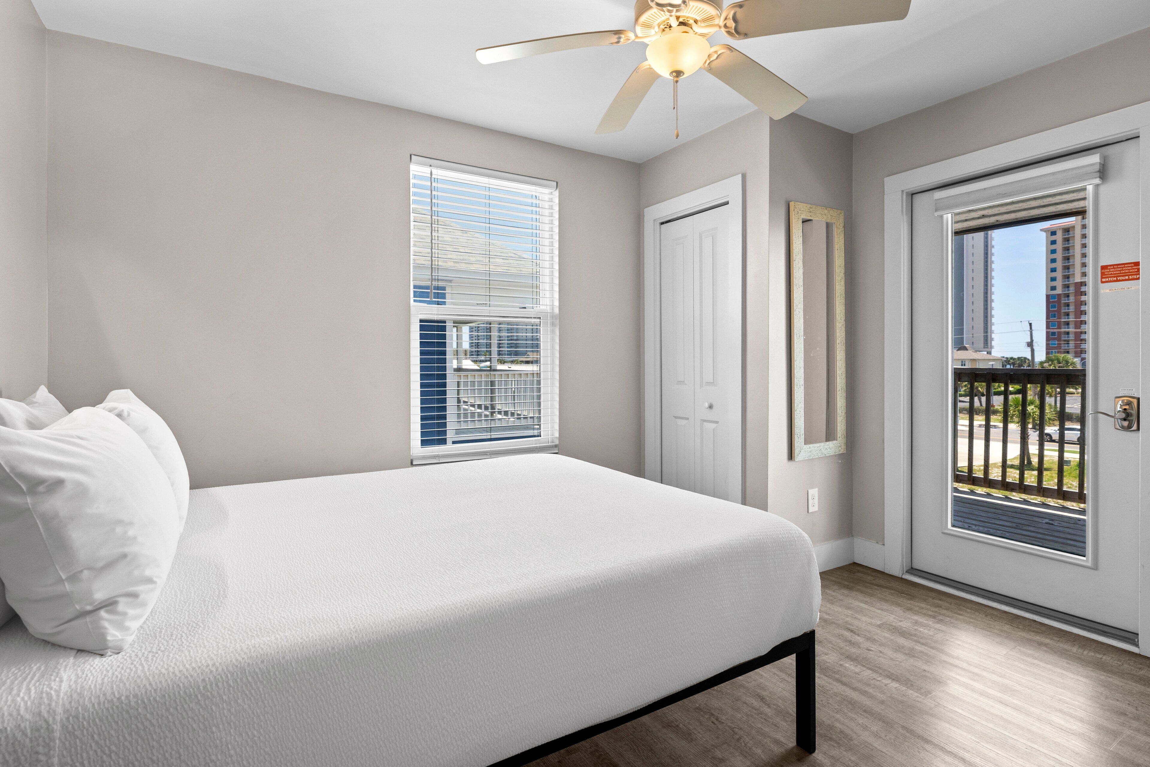 A bedroom with a bed, a ceiling fan, a door, and a window.