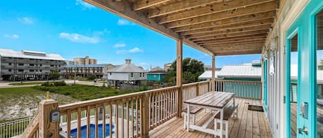 A wooden deck with a pool, a table, and a view of other buildings.