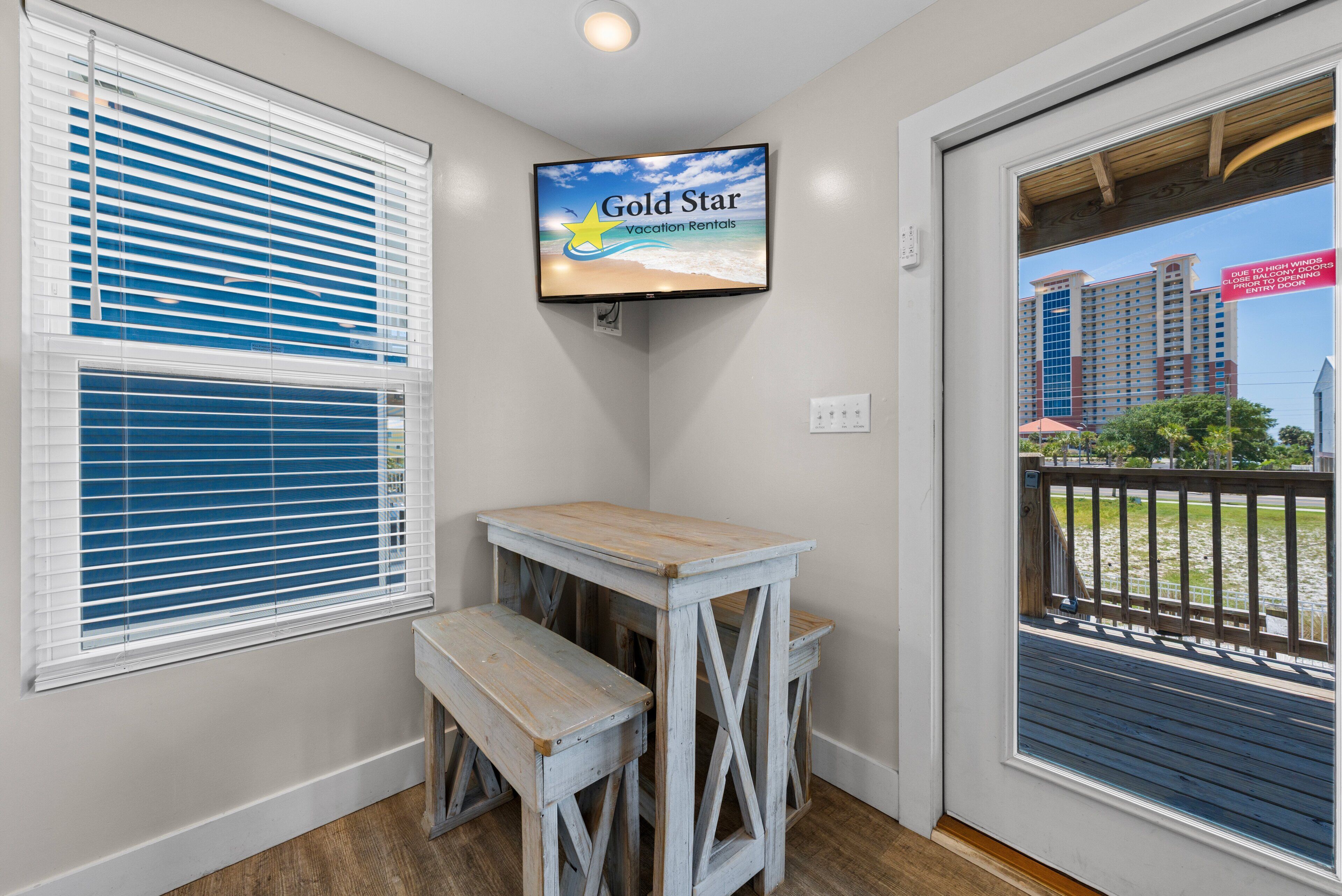 A room with a television displaying 'Gold Star Vacation Rentals,' a wooden bench, and a view of a beach through a door.
