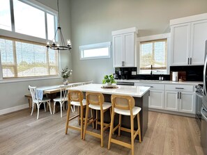 A modern kitchen with white cabinetry, a central island with seating, and a chandelier. - Hot Tub · Arcade · Sleeps 11 · Walk Downtown/Beach (Ocean Shores)
