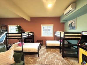 A dormitory room with bunk beds, a small table, a potted plant, and a window. - Hot Tub · Arcade · Sleeps 11 · Walk Downtown/Beach (Ocean Shores)