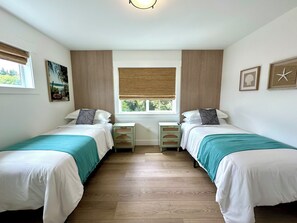 A room with two single beds, a window with blinds, a bedside table with drawers, and a wall-mounted light fixture. - Hot Tub · Arcade · Sleeps 11 · Walk Downtown/Beach (Ocean Shores)