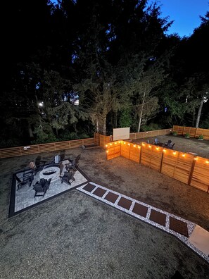 Een terras buiten met vuurkorf, zitplaatsen en lichtjes.