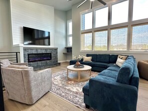 A modern living room with a fireplace, a large flat-screen TV, a sectional sofa, and a coffee table. - 2 Houses · Arcade · Speakeasy · Sauna · Sleeps 20 (Ocean Shores)