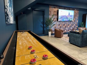 Een pooltafel met genummerde vakken, een televisie bevestigd aan een patroonmuur, en een bank in een kamer met donkere muren.