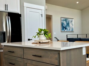 A modern kitchen with a marble countertop, wooden drawers, and a potted plant on a wooden coaster. - 2 Houses · Arcade · Speakeasy · Sauna · Sleeps 20 (Ocean Shores)
