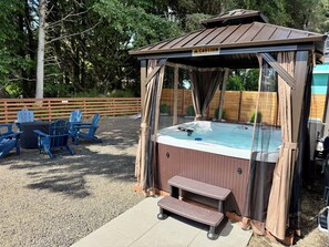 A hot tub with a canopy, surrounded by outdoor seating and a wooden fence. - 2 Houses · Arcade+Speakeasy · Sleep 20 · 100" TV (Ocean Shores)