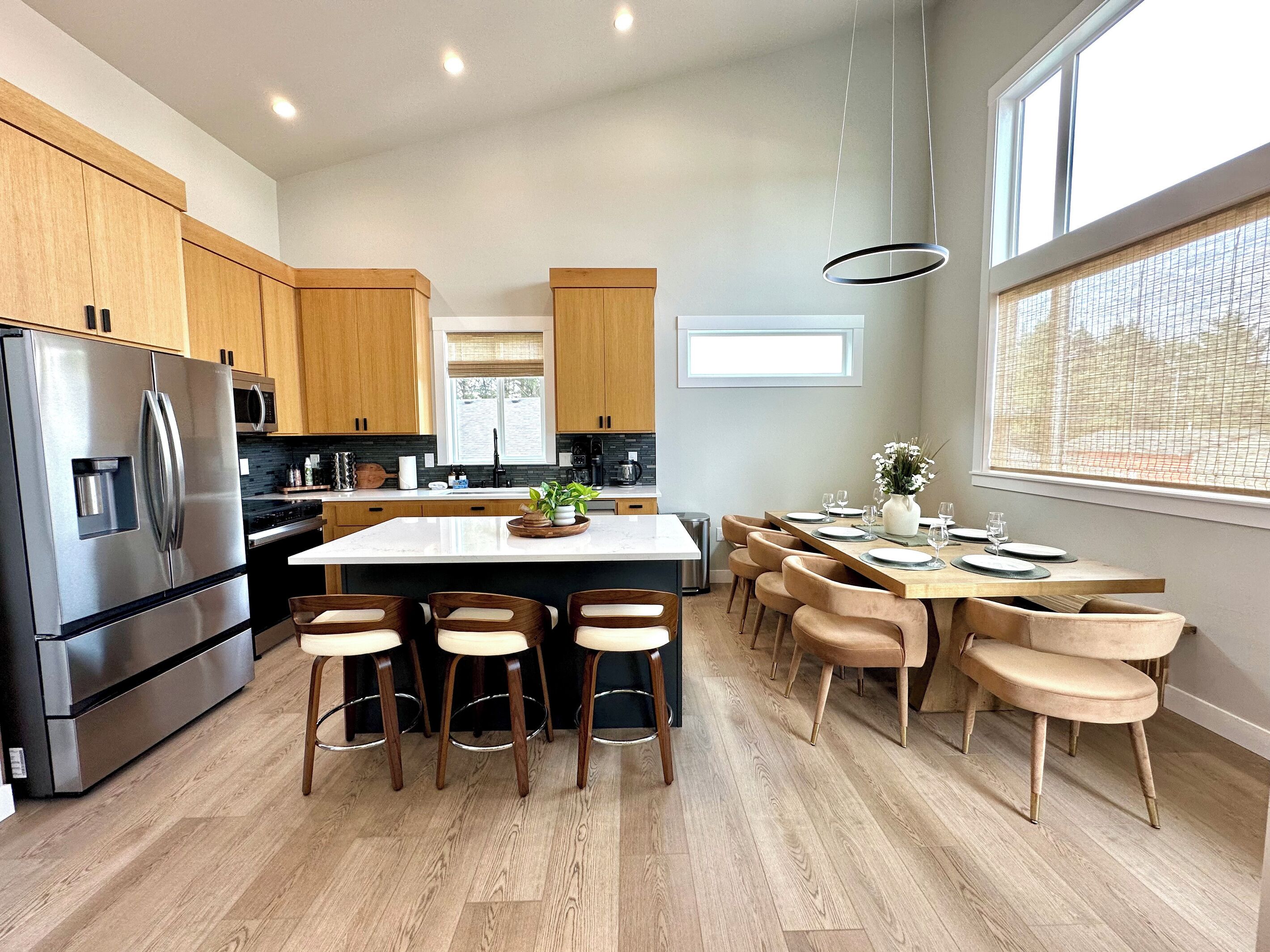 Una cocina moderna con una isla central, armarios de madera, electrodomésticos de acero inoxidable y un comedor con sillas y una mesa.