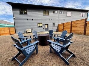 Een grijs gebouw met een terras, compleet met vier Adirondack-stoelen en een ronde tafel.