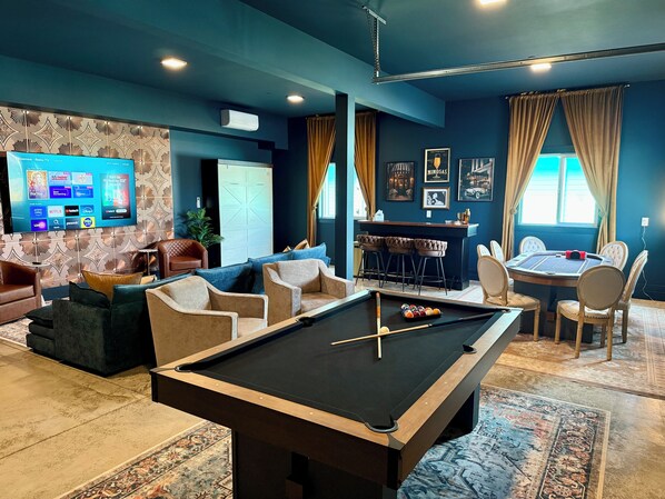 A pool table in a room with a sofa, chairs, a bar area, and a television displaying a streaming service interface. - Hot Tub+Speakeasy · Sleeps 9 · Walk Downtown/Beach (Ocean Shores)