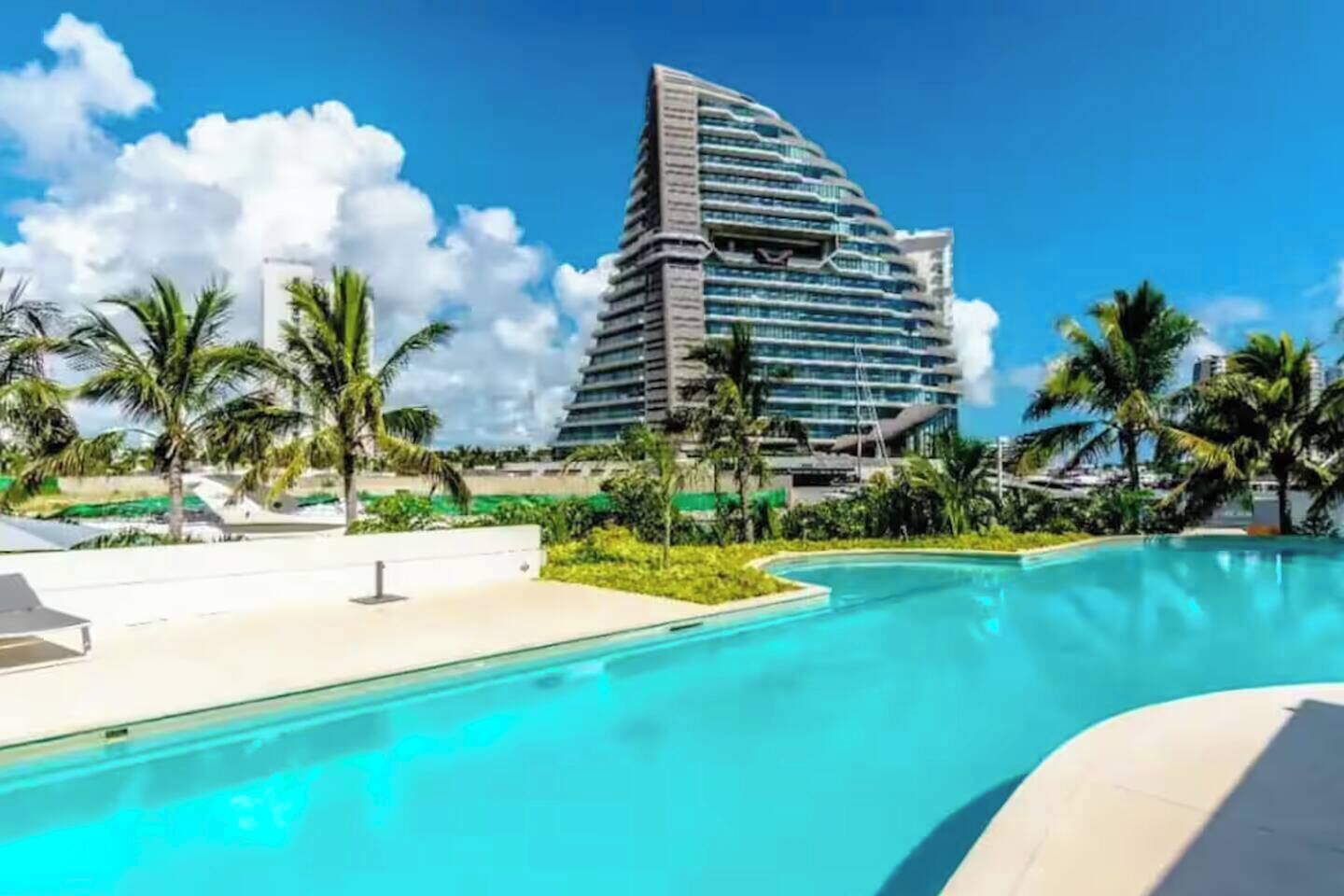 Ein modernes Hotel mit Pool, Palmen und blauem Himmel.