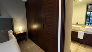 Hotelkamer met een bed, nachtkastje, lamp, kledingkast en een badkamer met wastafel en spiegel.