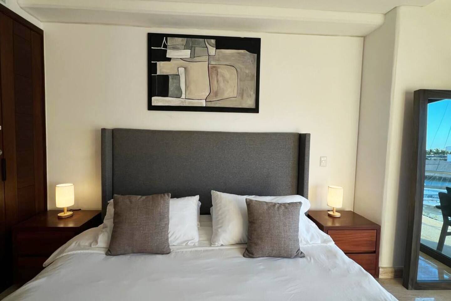 Ein Hotelzimmer mit einem großen Bett, zwei Nachttischen, einem Wandbild im abstrakten Stil und einem Fenster mit Blick.