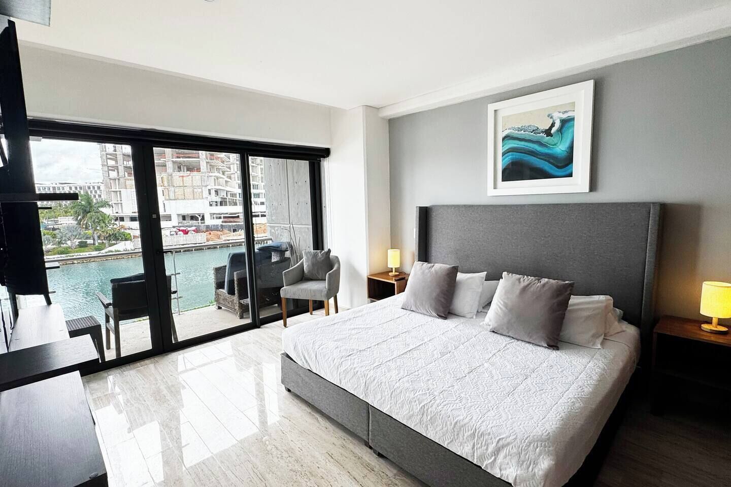 Une chambre d’hôtel moderne avec un grand lit, un bureau et une vue sur une étendue d’eau, accessible par une porte-fenêtre coulissante.