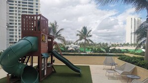 A playground with a slide and climbing structure, surrounded by outdoor seating and palm trees. - TOP/1BR/Contemporary Condo/Huge Terrace/Gym/HZ (Cancún)