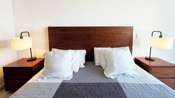 Een hotelkamer met een groot bed, twee nachtkastjes met lampen en een houten hoofdeinde.