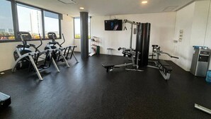 Ein Fitnessstudio mit diversen Trainingsgeräten, großen Fenstern und einem Flachbildfernseher.