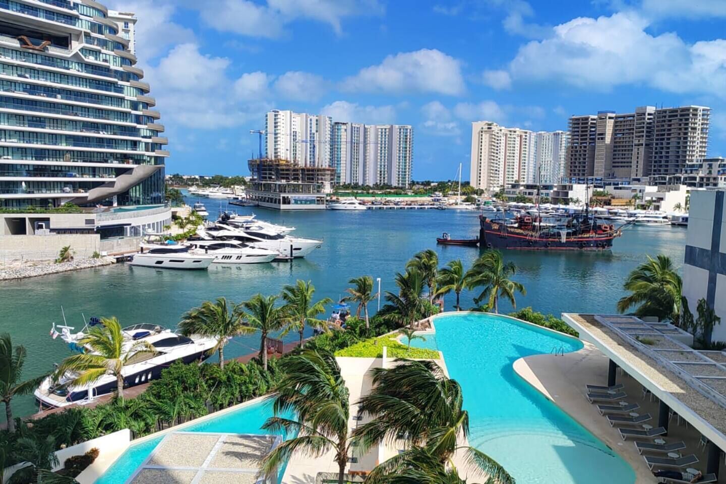 Marina con yates, piscina y edificios altos al fondo.
