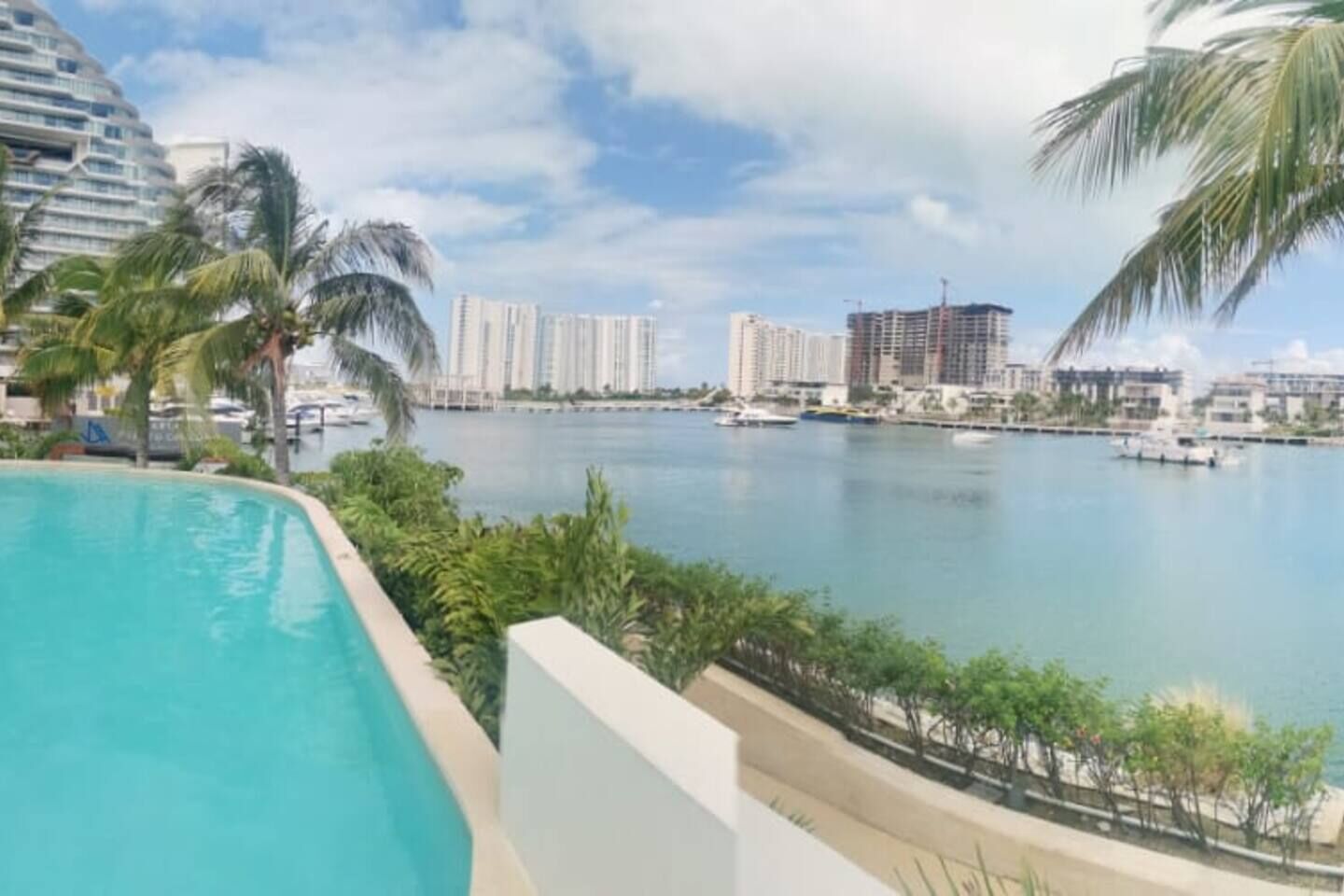 A poolside view overlooking a marina with boats, palm trees, and high-rise buildings in the background.