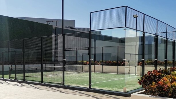 Ein Tennisplatz, umgeben von einer Glasumrandung und mit einem grünen Kunstrasenbelag.