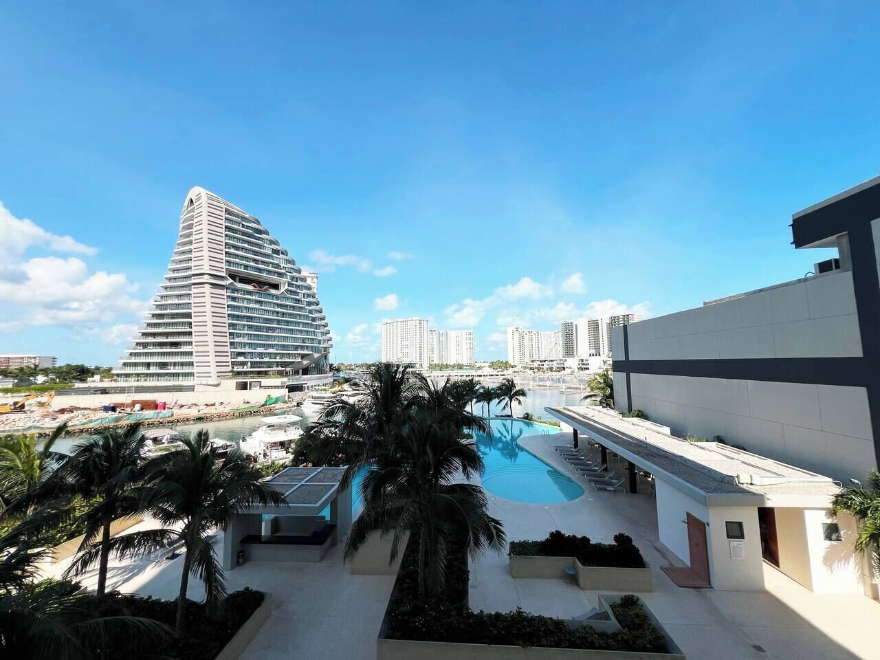 Ein modernes Hotel mit Pool, Palmen und Blick auf ein hohes Gebäude.