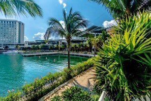 Un hotel frente al mar con piscina, palmeras y vista al horizonte de la ciudad.