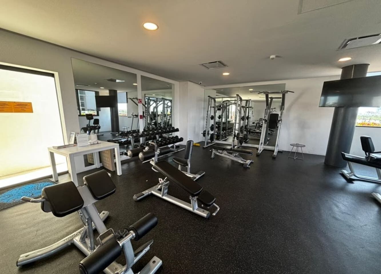 Ein Fitnessstudio mit unterschiedlichen Trainingsgeräten, Spiegeln und einem schwarzen Boden.