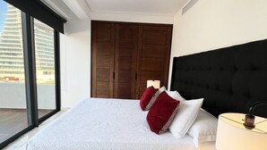 Ein Hotelzimmer mit einem großen Bett, einer dunklen Kopfteil und Blick auf ein Gebäude durch ein Fenster.