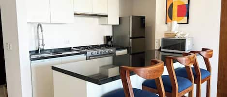 A modern kitchen with white cabinets, a black countertop, and a central island with bar stools.