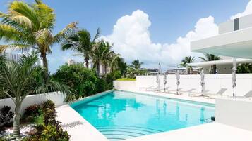 Une piscine entourée de palmiers et de verdure, avec des chaises longues et des parasols.